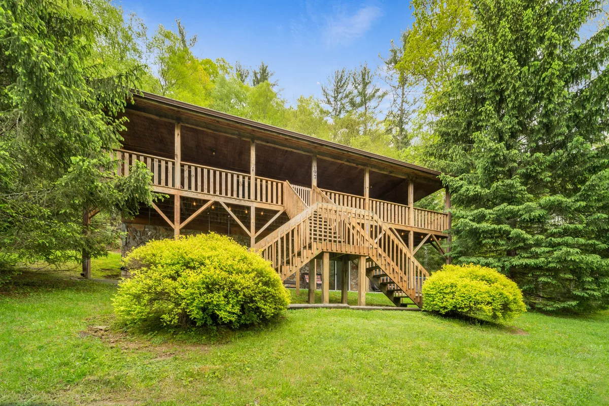 A wooden deck surrounded by lush greenery and bushes is showcased in this exterior shot. Stairs lead from the deck into the yard, and the tranquil atmosphere suggests a great spot for morning coffee or relaxing after a day of adventure.