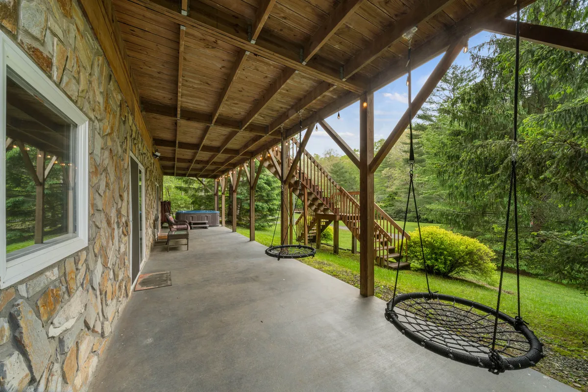 Hanging rope swings are suspended from a sturdy structure, with a stone wall and lush greenery providing a playful and tranquil backdrop. The swings overlook a gently sloping yard, ideal for kids and pups to play.