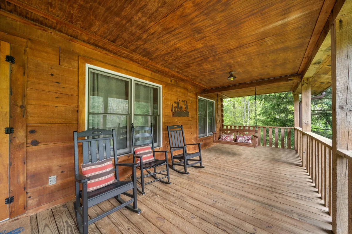 A pair of classic wooden rocking chairs rest on a covered deck, facing out toward a vista of rich greenery. The calm setting invites guests to relax, read, or simply enjoy the fresh mountain air.