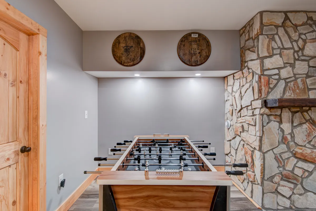 A cozy entertainment area with a foosball table as the main feature, complemented by a rustic stone wall and wooden barrels that add character. The space feels lively, perfect for playful competitions and group enjoyment.