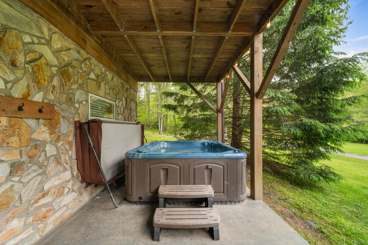 This image features a bubbling hot tub surrounded by wooden beams and lush greenery, with a stone wall adding a rustic touch. The setting exudes tranquility and invites guests to relax outdoors while soaking in mountain views.